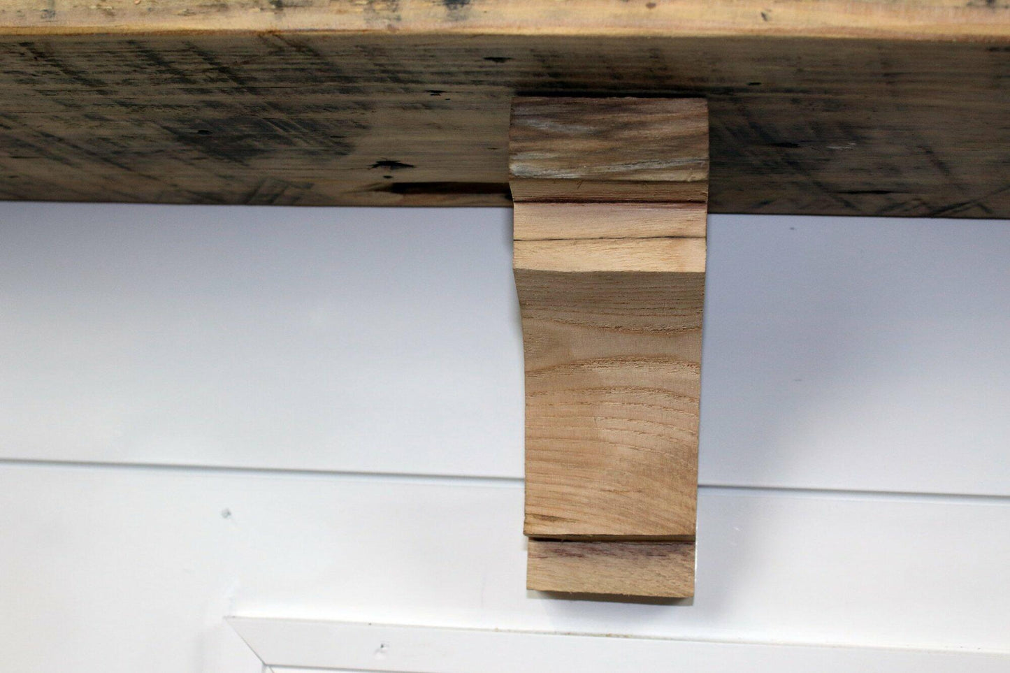 decorative corbel made from reclaimed barnwood in a frontal view. Wood grain displayed and the corbel is shown in a decorative profile. There is one medium step at the top of the corbel before the arch and one at the bottom as well.