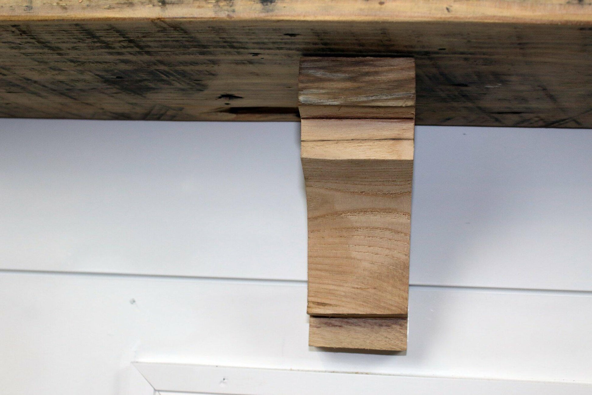 decorative corbel made from reclaimed barnwood in a frontal view. Wood grain displayed and the corbel is shown in a decorative profile. There is one medium step at the top of the corbel before the arch and one at the bottom as well.