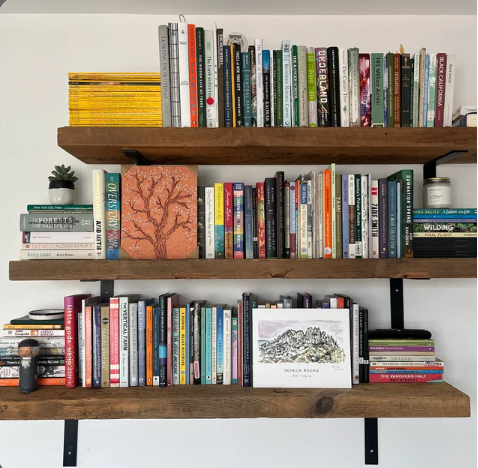 three reclaimed barn wood wall shelves shown with visible angle brackets. Shelves are shown without a finish applied and covered in books.