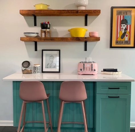 two reclaimed barnwood wall shelves shown over a retro style breakfast nook. Shelves are shown in the oil finish with variations of the wood grain and nail holes displayed. The shelves are decorated with kitchenware in complimentary pastel colors to the rest of the room.