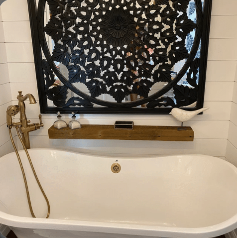 reclaimed barnwood floating shelf shown on a shiplap wall over a bathtub. The natural finish compliments the light colors in the room and contrasts the wall decor mounted above it.