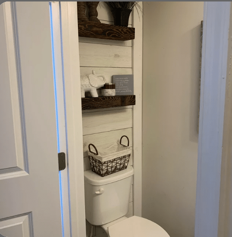 two reclaimed barnwood floating shelves on a wood wall in a bathroom. Shelves are mounted above a toilet with the grain pattern very prominent on the face of the shelves.