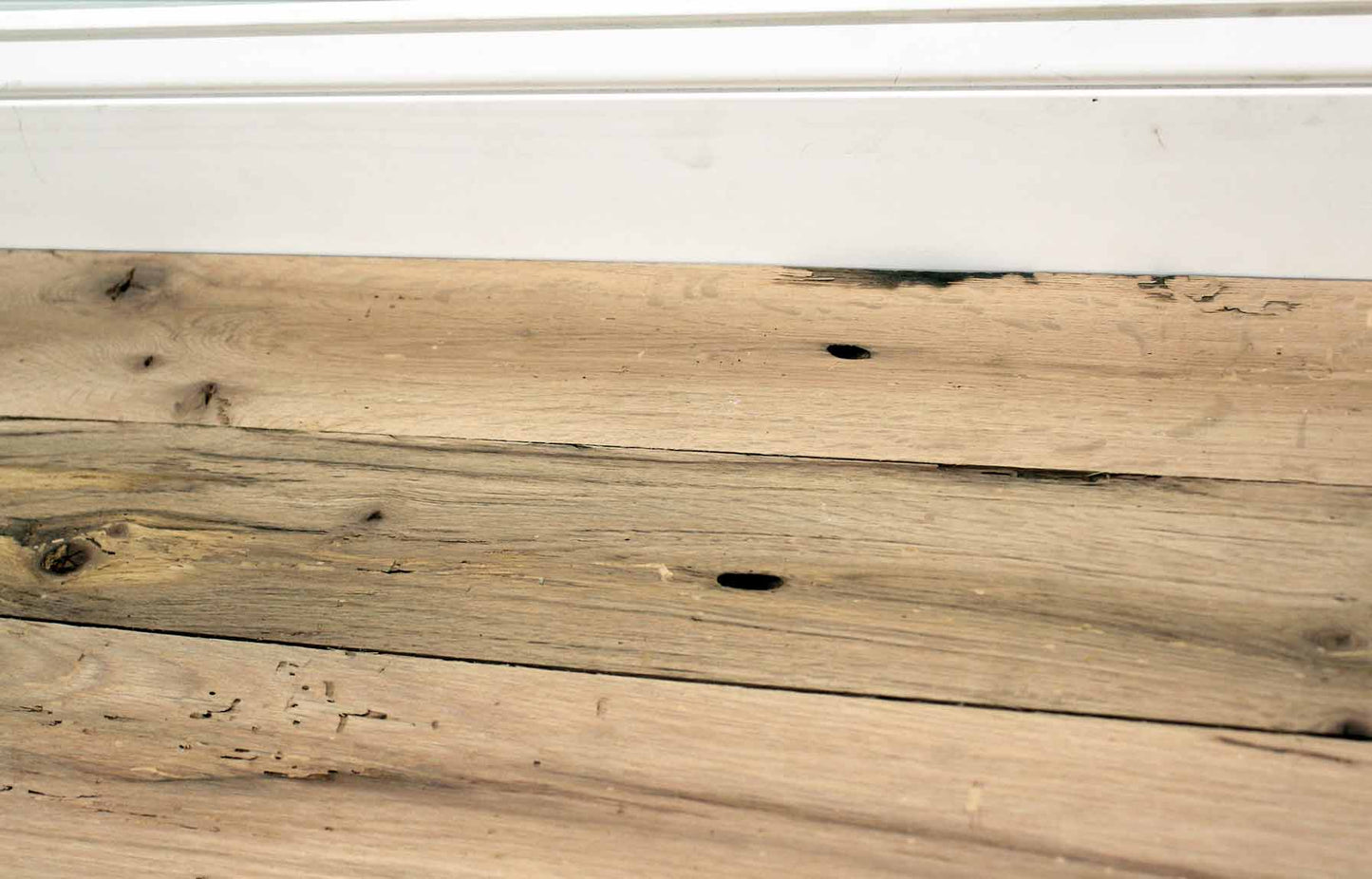 red oak reclaimed flooring installed with baseboard molding. Variations in wood color and grain pattern, knots, and characteristics from previous bug activity shown.
