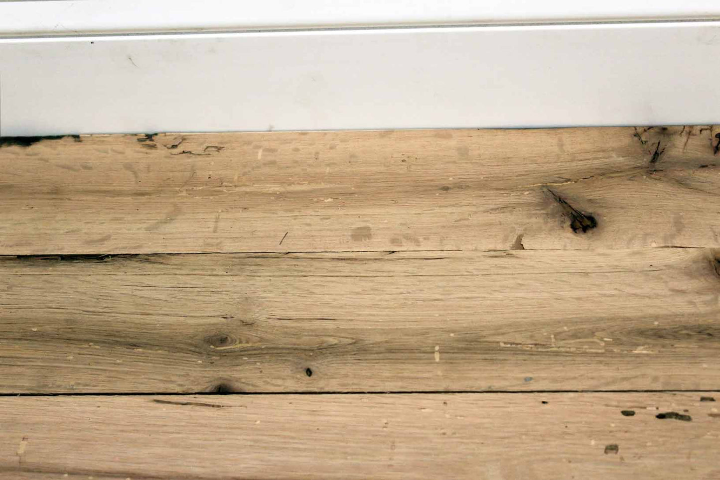 red oak reclaimed flooring installed with baseboard molding. Variations in wood color and grain pattern, knots, and characteristics from previous bug activity shown.