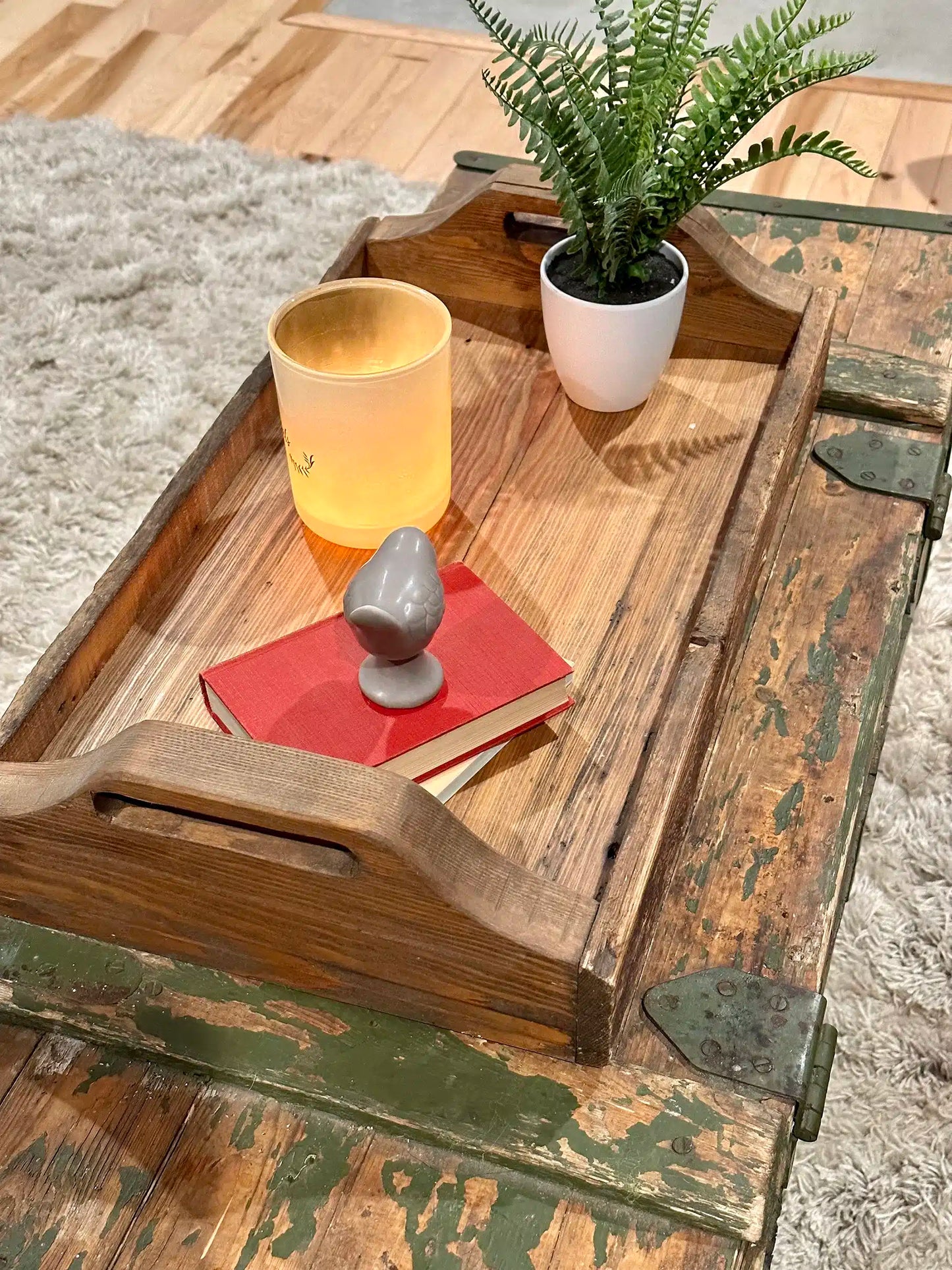 wood serving tray in a top down view from slightly further away displayed on an old army chest. Shows rounded handles, characteristics in the wood, and decor items placed on top.