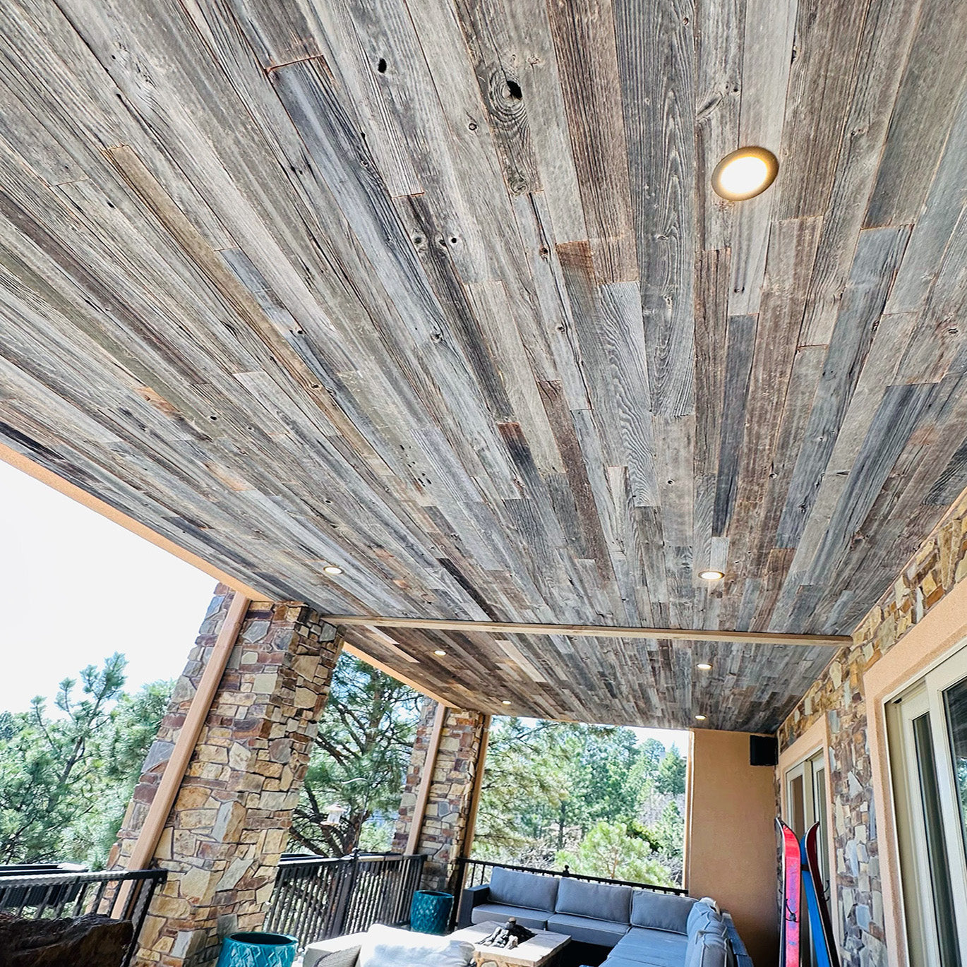 weathered grey barnwood paneling installed on a ceiling of an outdoor sunroom. Variations of color, texture, and characteristics displayed throughout.