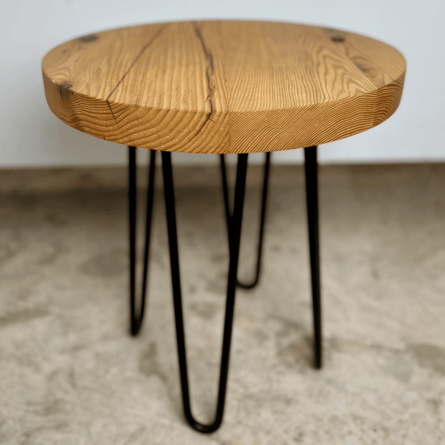 a reclaimed wood table in an round shape and sealed unfinished finish. The table is supported by four hairpin legs. Checking and grain patterns present in the wood.