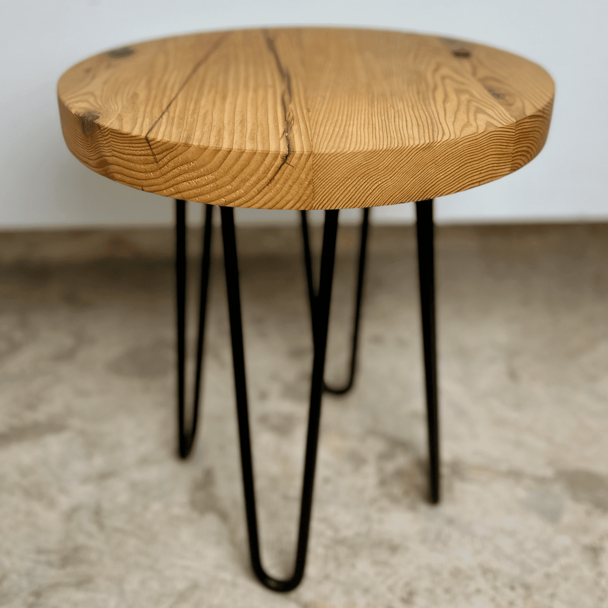 a reclaimed wood table in an round shape and sealed unfinished finish. The table is supported by four hairpin legs. Checking and grain patterns present in the wood.