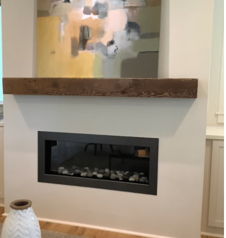 a reclaimed wood fireplace mantel mounted over a fireplace. The grain pattern and knots are displayed in the front face of the mantel.