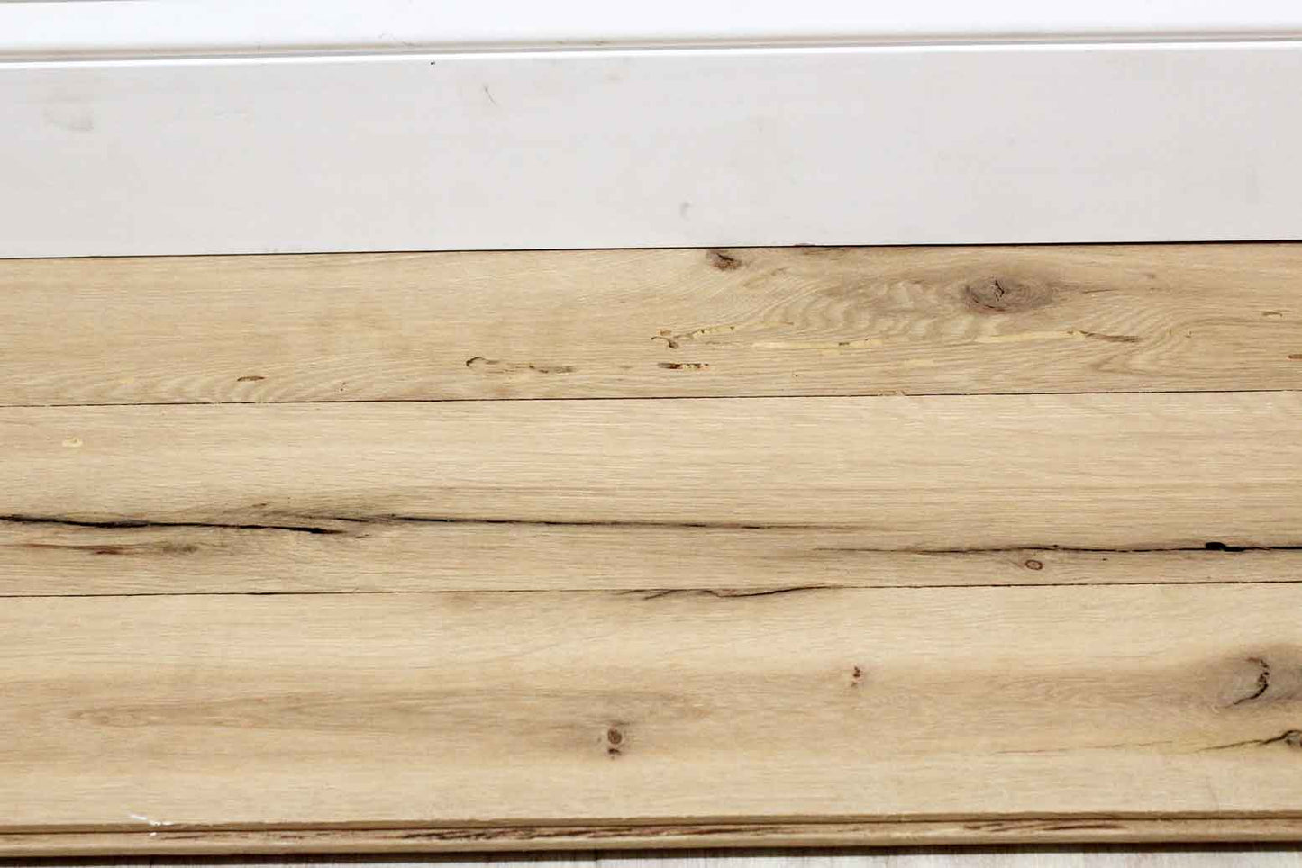 reclaimed white oak flooring installed with baseboard molding. Variations in wood color shown along with knots, checking, and characteristics from previous bug activity.