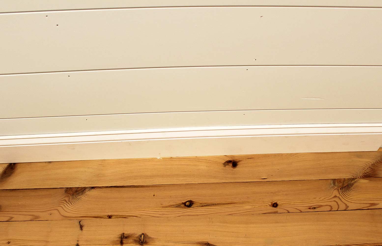 yellow pine reclaimed wood flooring installed with baseboard. Flooring shows knots and prominent grain patterns.
