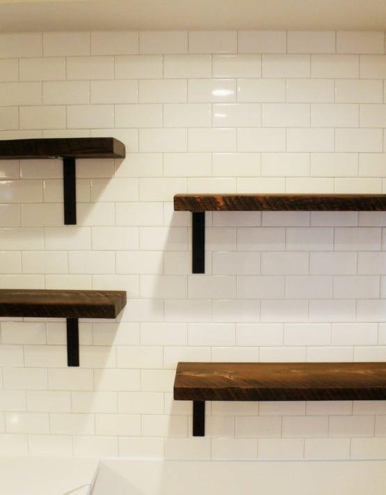 four reclaimed wood wall shelves staggered on a subway tile wall in a kitchen. Shelves are not decorated but shown in the early american finish.