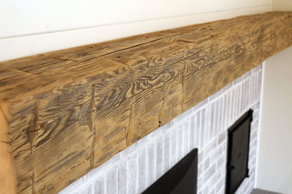 close up of a natural wood colored, hand hewn beam showing the woods grain patterns on a light colored fireplace. Mantel shows natural characteristic called checking which is similar to cracking, axe marks, and grain patterns.