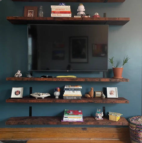 four reclaimed barnwood wall shelves shown in the oil finish. One shelf is mounted above a television while three shelves are mounted below the television to the floor spaced evenly apart.