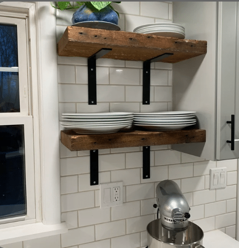 two reclaimed barnwood wall shelves shown in the natural option. Shelves are shown in a kitchen mounted on subway tile holding plates. Nail holes are prominently displayed on the face of the shelves.