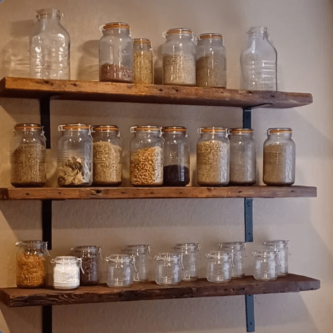 three reclaimed wood wall shelves shown in the natural option. Shelves are adorned with various sized glass jars holding herbs and spices. Nail holes and grain patterns are displayed across the face of the shelves.