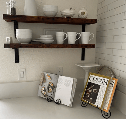 two reclaimed barnwood wall shelves shown in a kitchen corner. Nail holes are prominently displayed across the face of the shelves. Shelves are displaying mugs, bowls, and other kitchenware's. Dark coloration of shelves provides a contrast to surrounding decor. 