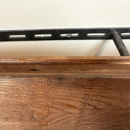 a close up of the back of a reclaimed wood floating shelf. There is a bracket mounted onto the wall with a peg protruding, and the back of the shelf to demonstrate installation.