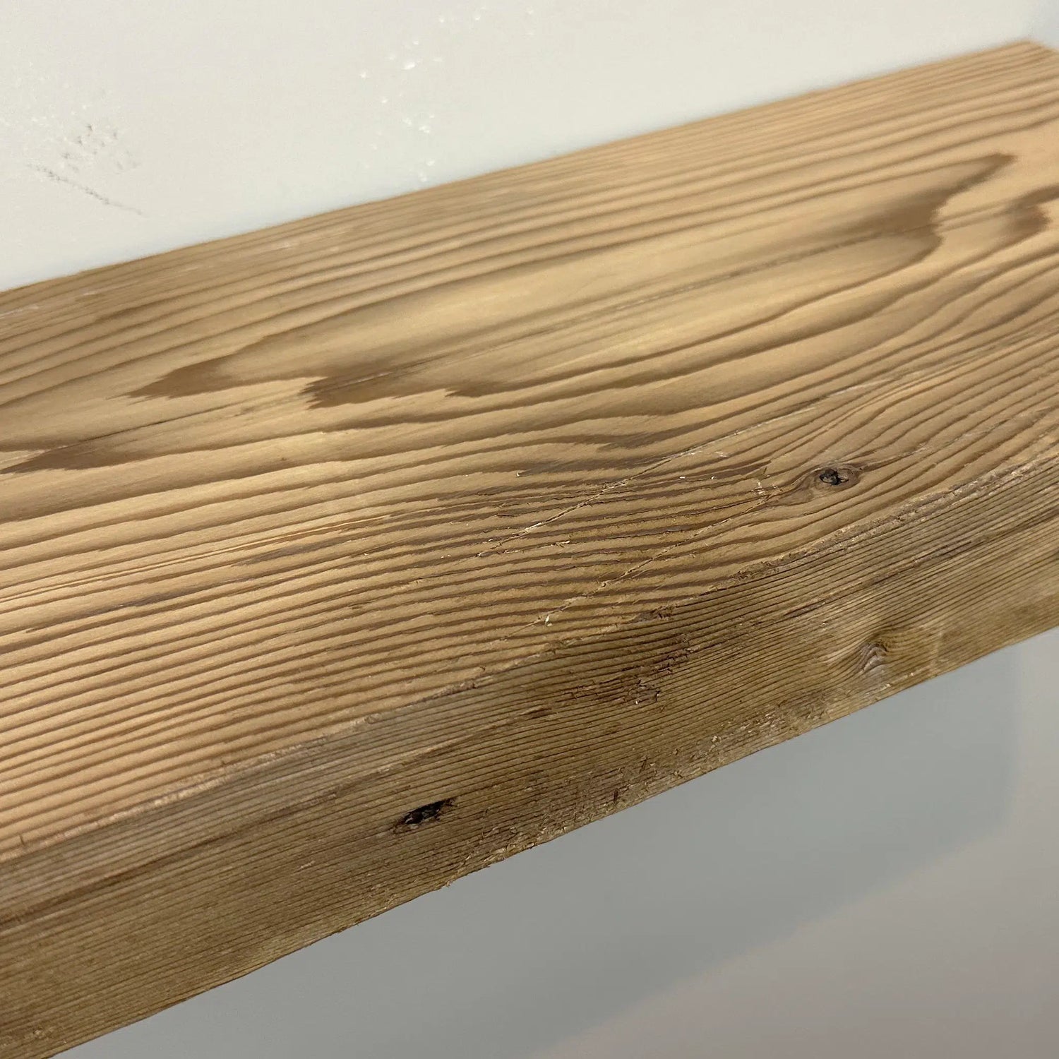 a close up of a reclaimed wood floating shelf in the natural option. Grain pattern, knots, and nail holes are present in the wood.