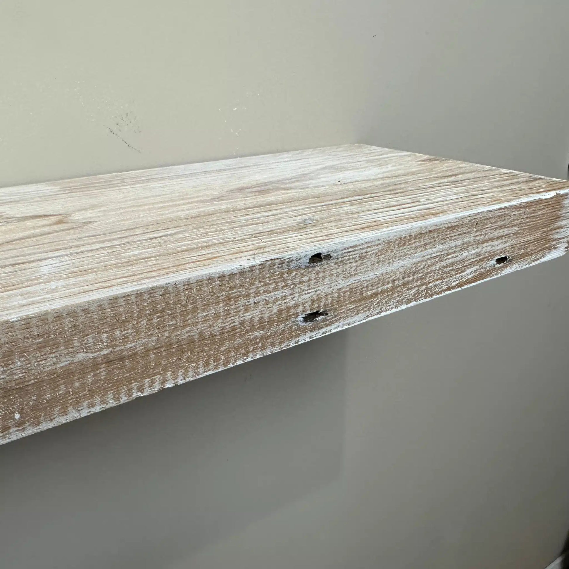 a close up of a reclaimed wood floating shelf in the white wash option. White wash application and nail holes are shown in the wood.