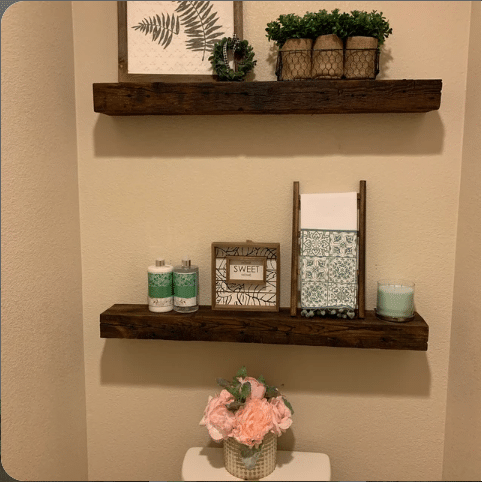 two reclaimed barnwood floating shelves on a wall in a bathroom. Shelves are mounted above a toilet with nail holes and grain patterns displayed.