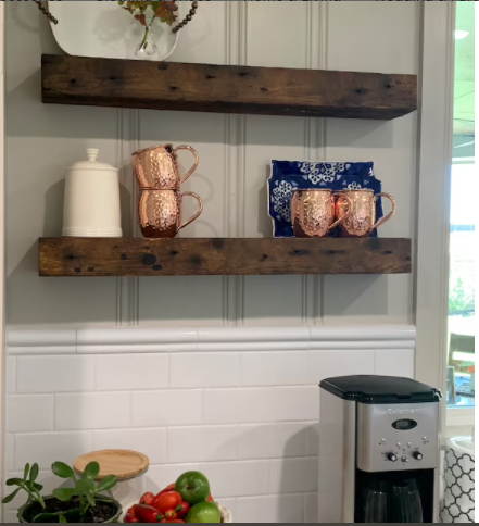 two reclaimed barnwood floating shelves shown in a kitchen. Face of shelves shows nail holes and variations in color from the oil finish. Copper mugs decorate the bottom shelf.