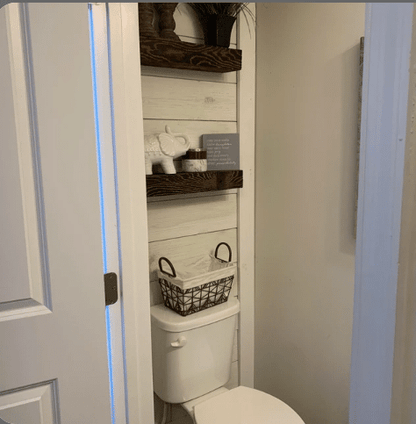 two reclaimed barnwood floating shelves on a wood wall in a bathroom. Shelves are mounted above a toilet with the grain pattern very prominent on the face of the shelves.