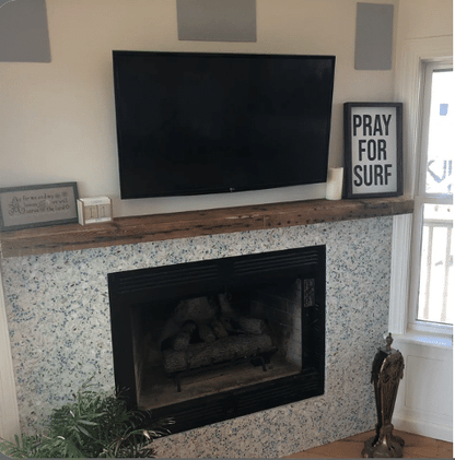 a reclaimed wood floating fireplace mantel showing in the natural finish. Checking/cracking, nail holes, and variations of wood color are present in the mantel.