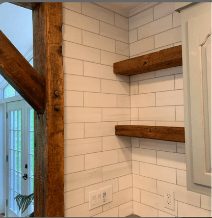 two reclaimed wood floating shelves shown in the natural option. Shelves are mounted in a corner with a matching reclaimed door frame in view that matches.