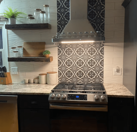 two reclaimed wood floating shelves shown in a kitchen. Shelves are mounted to the left of a stove and a range hood holding various sized jars.