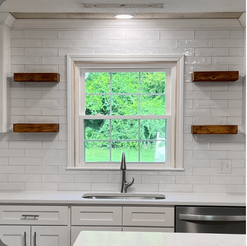 four reclaimed wood floating shelves shown in a kitchen in the oil finish. Two shelves are mounted on either side of a window which is above a sink.