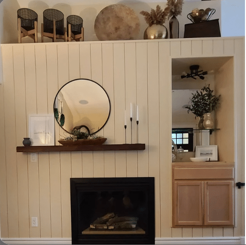reclaimed wood floating fireplace mantel shown in the oil finish. Mantel is shown mounted on a fireplace wall with a round mirror over top.