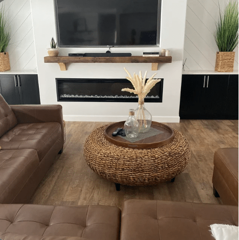 a reclaimed wood floating fireplace mantel in the natural option. Mantel is shown in a living room mounted over a fireplace and below a television. The mantel has matching corbels shown underneath and compliments the other colors in the room. 