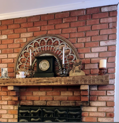 a reclaimed wood floating fireplace mantel in the natural option. The mantel is mounted on a traditional brick fireplace and on top of brick corbels. Nail holes, lath lines, and wood color variation are present in the mantel.