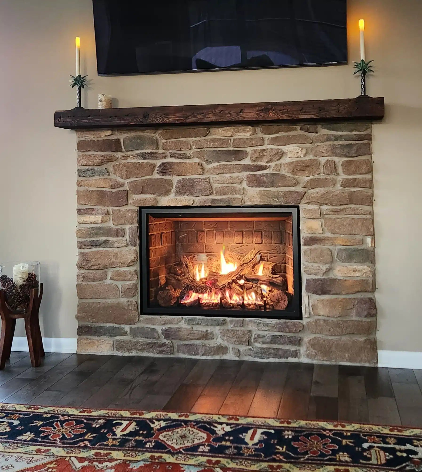 a reclaimed wood floating fireplace mantel in the oil finish. the mantel is mounted above a stone fireplace surround with a lit fire underneath.