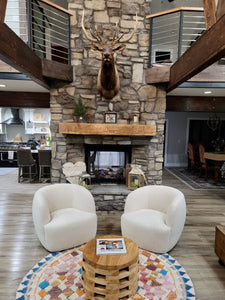 Reclaimed Wood Mantel in common area with white chairs and deer head mounted over fireplace with wood beams 