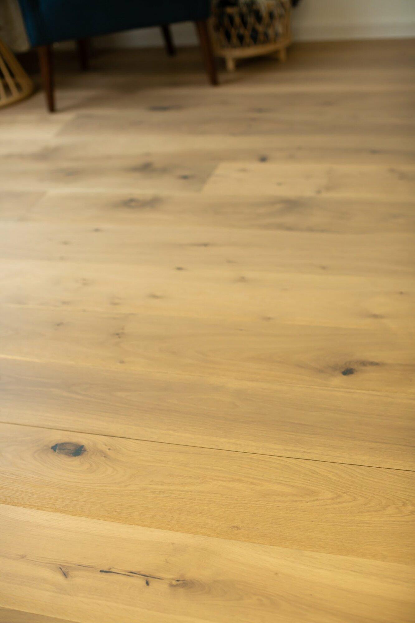 close up of engineered white oak wide plank flooring. With a UV Lacquer Matte finish, the ends of each piece are tongue and grooved for an easy install. Each piece of flooring shows knots and other subtle variations. This finished engineered hardwood has square edges and square ends.