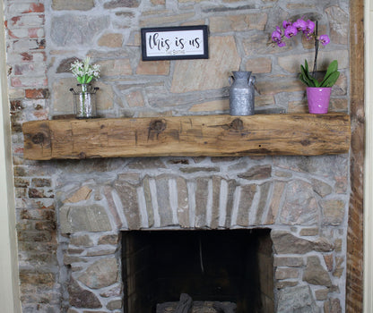natural wood colored, hand hewn beam showing the woods grain patterns and prominent knots on a light stone fireplace. Mantel has light axe marks across the front.
