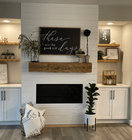 natural wood colored, hand hewn beam showing the woods grain patterns on a light shiplap fireplace. Mantel shows natural characteristic called checking which is similar to cracking. Hand hewn mantel is flanked by four, 2" thick shelves over cabinets.