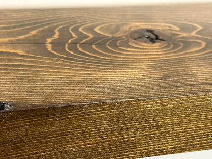 a close up of the finish on a reclaimed wood floating shelf in the contemporary collection. The lacquer application adds a shine and smoothness to the wood. Grain pattern, and knots are present and highlighted in the wood.