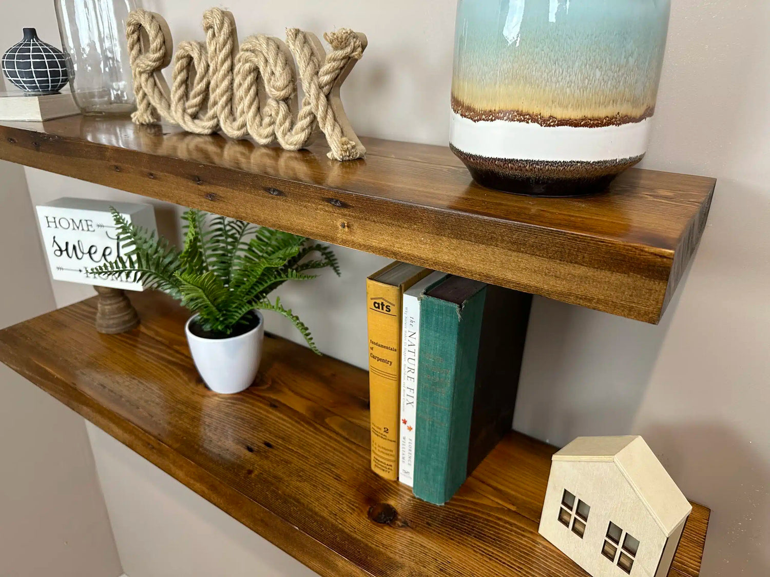 two reclaimed wood floating wall shelves in the contemporary collection and early american finish. Shelves have a shine on them from a lacquer application and show variance in wood color, grain pattern, knots, and nail holes in the wood.