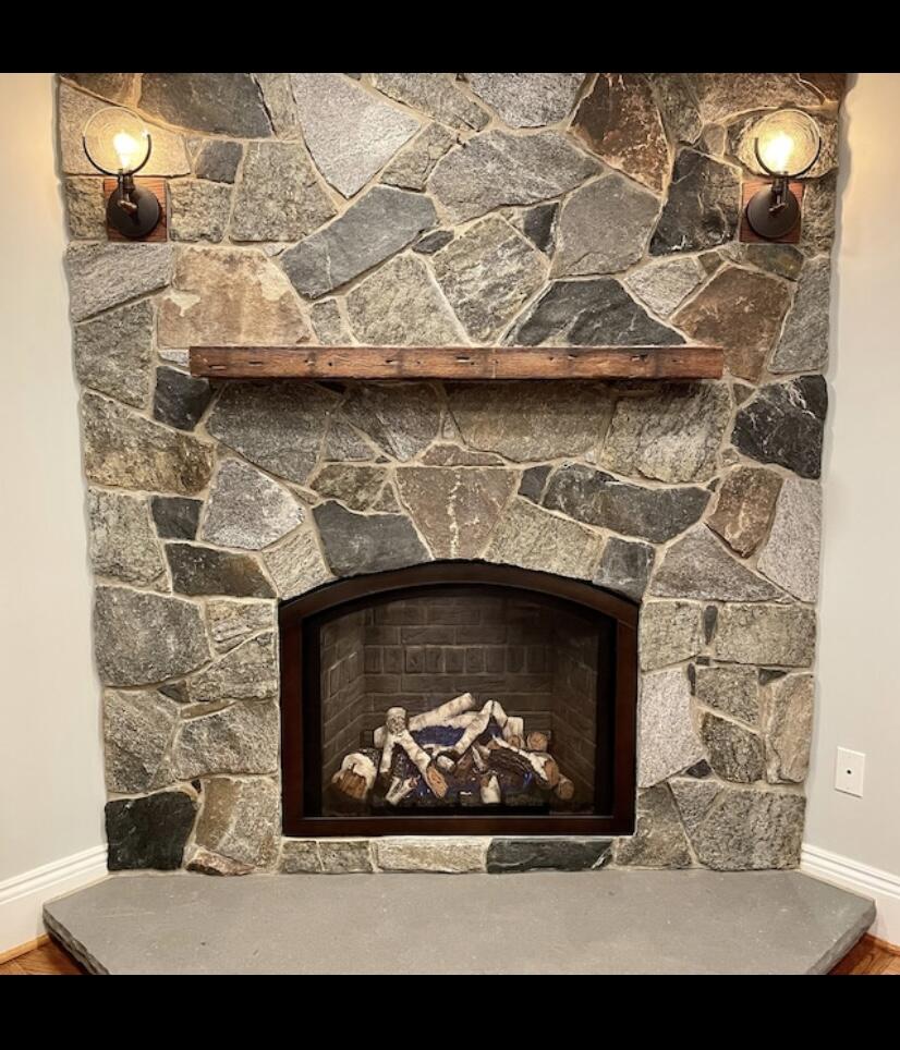 a reclaimed barnwood floating fireplace mantel. Shown natural on a stone fireplace with nail holes displayed.