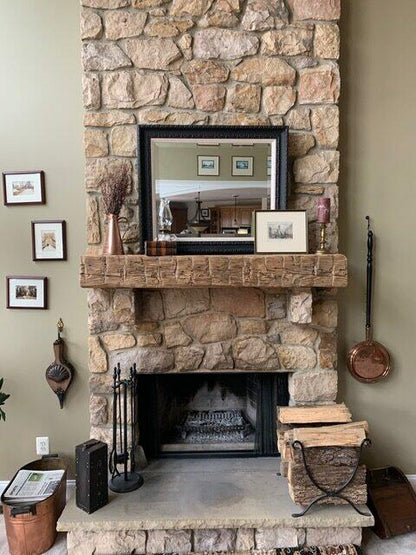 natural wood colored, hand hewn beam showing the woods grain patterns on a stone fireplace. Mantel has aggressive axe marks across the front and nail holes displayed.