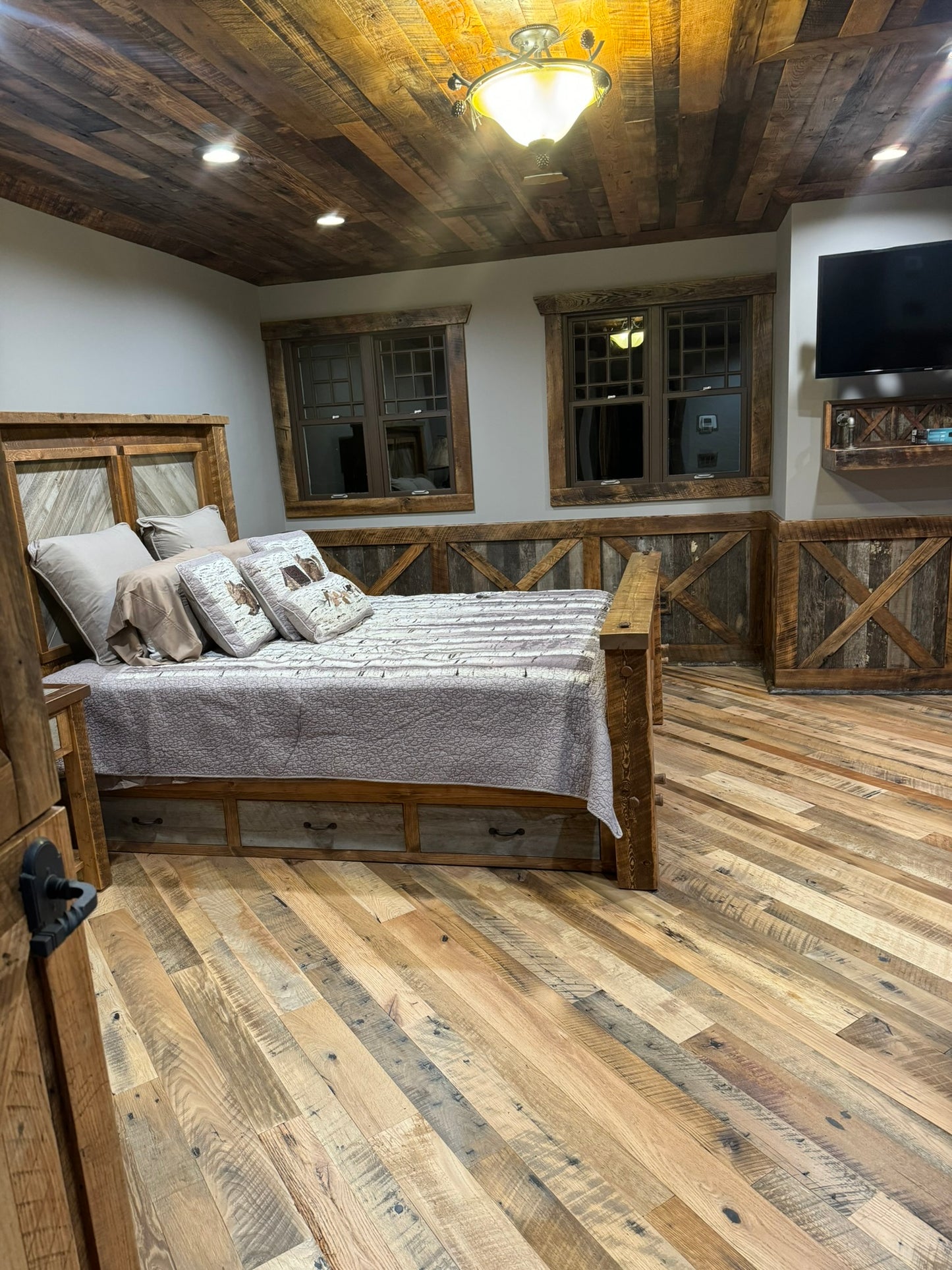 Heartland Barnwood Mixed Hardwoods Skip-Planed Brown flooring used in bed room with wood panel ceiling, wood wall trim with wood door and wood framed bed looking though door into room.