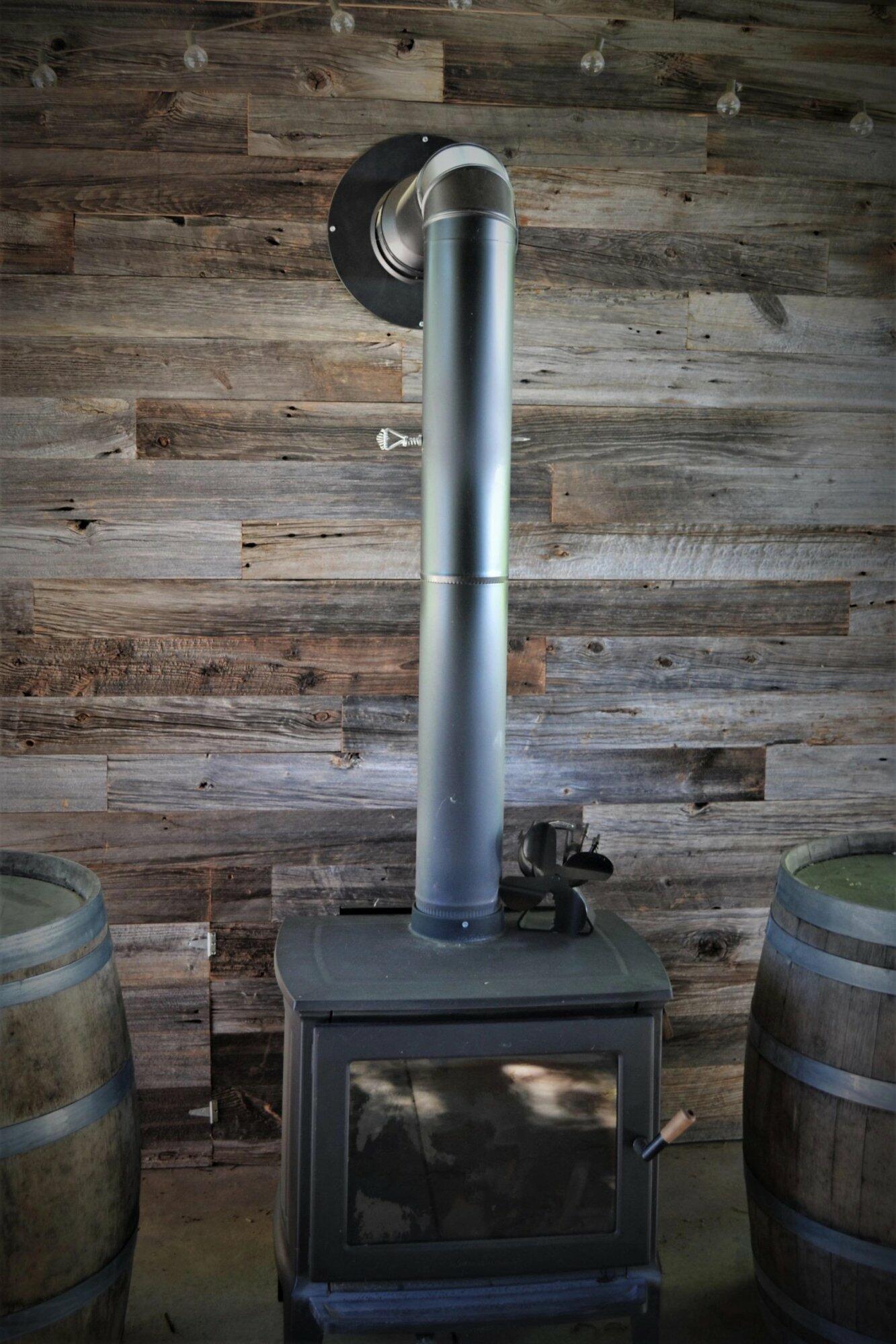 weathered grey barnwood paneling installed behind a wood stove. Variations of color, texture, and characteristics displayed throughout.