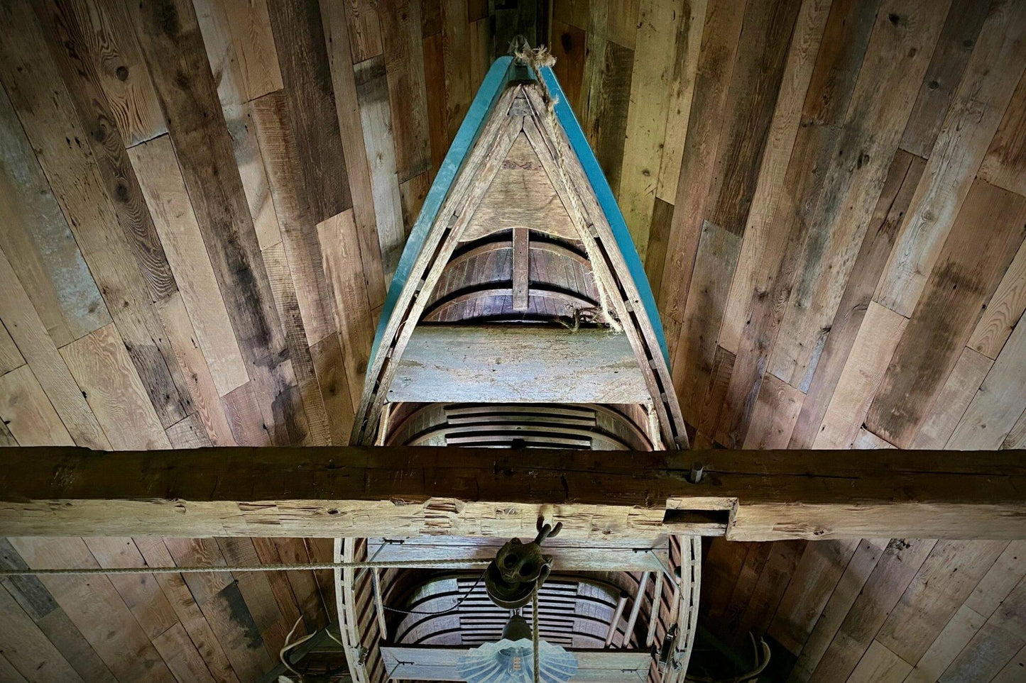 barnwood paneling on a ceiling at a wide angle. Barnwood paneling on wall is varied in width and length, showing many variations and characteristics. An old boat is mounting in the middle of vaulted ceiling.