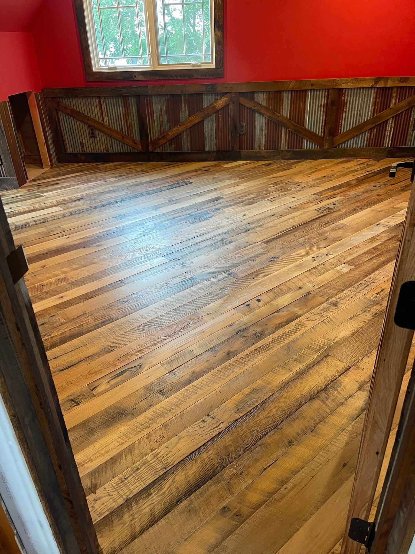 Close up of Heartland Barnwood Mixed Hardwoods Skip-Planed Brown flooring and red walls with wood wall trim in barn style room 