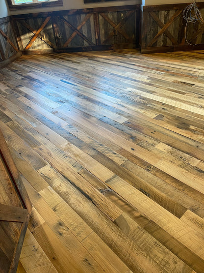 Close up of Heartland Barnwood Mixed Hardwoods Skip-Planed Brown flooring and wood wall trim in barn style room.