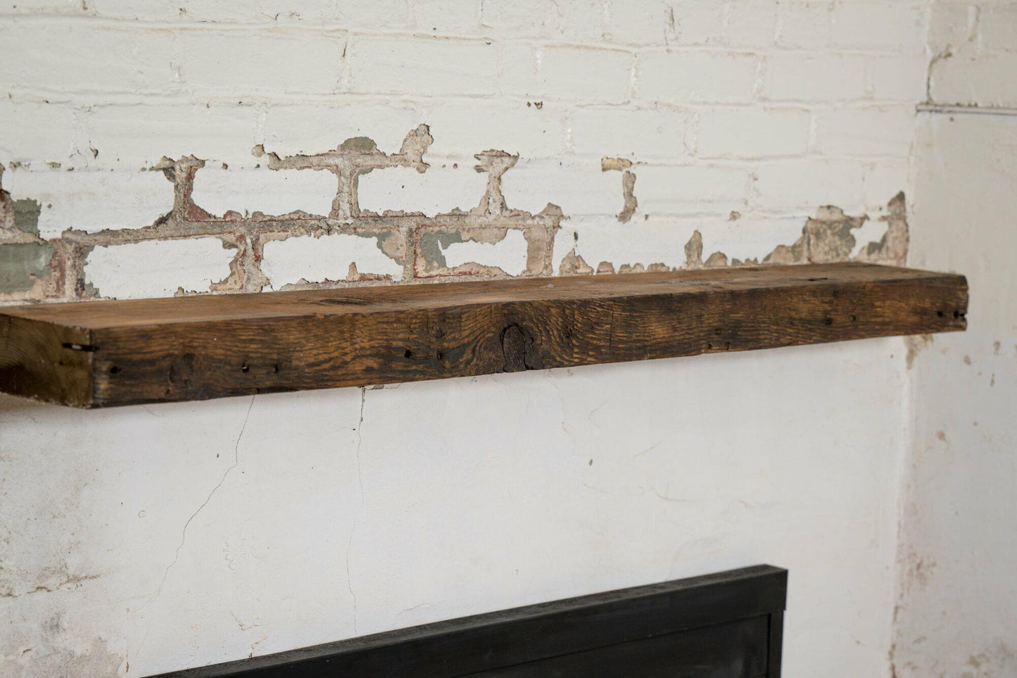reclaimed barnwood floating fireplace mantel in an oil finish. Displayed on a brick and concrete fireplace with knots, nail holes, and grain patterns present.