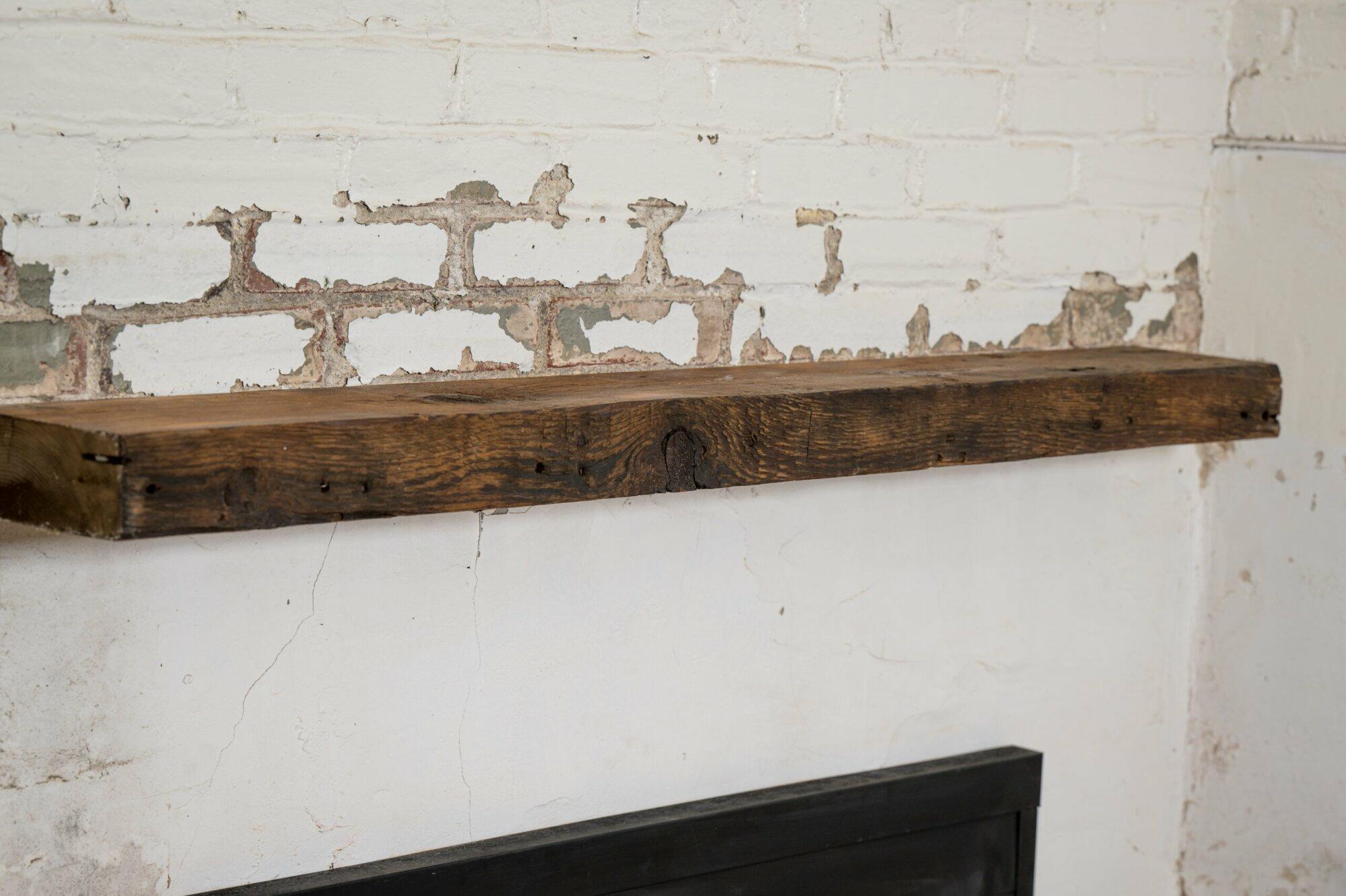 reclaimed barnwood floating fireplace mantel in an oil finish. Displayed on a brick and concrete fireplace with knots, nail holes, and grain patterns present.